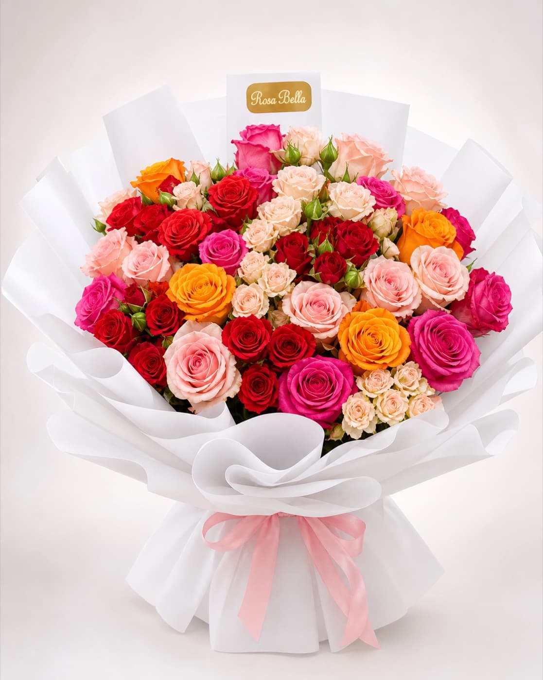 A wide bouquet of roses in red, pink, peach and orange, wrapped in white paper with a pink ribbon.