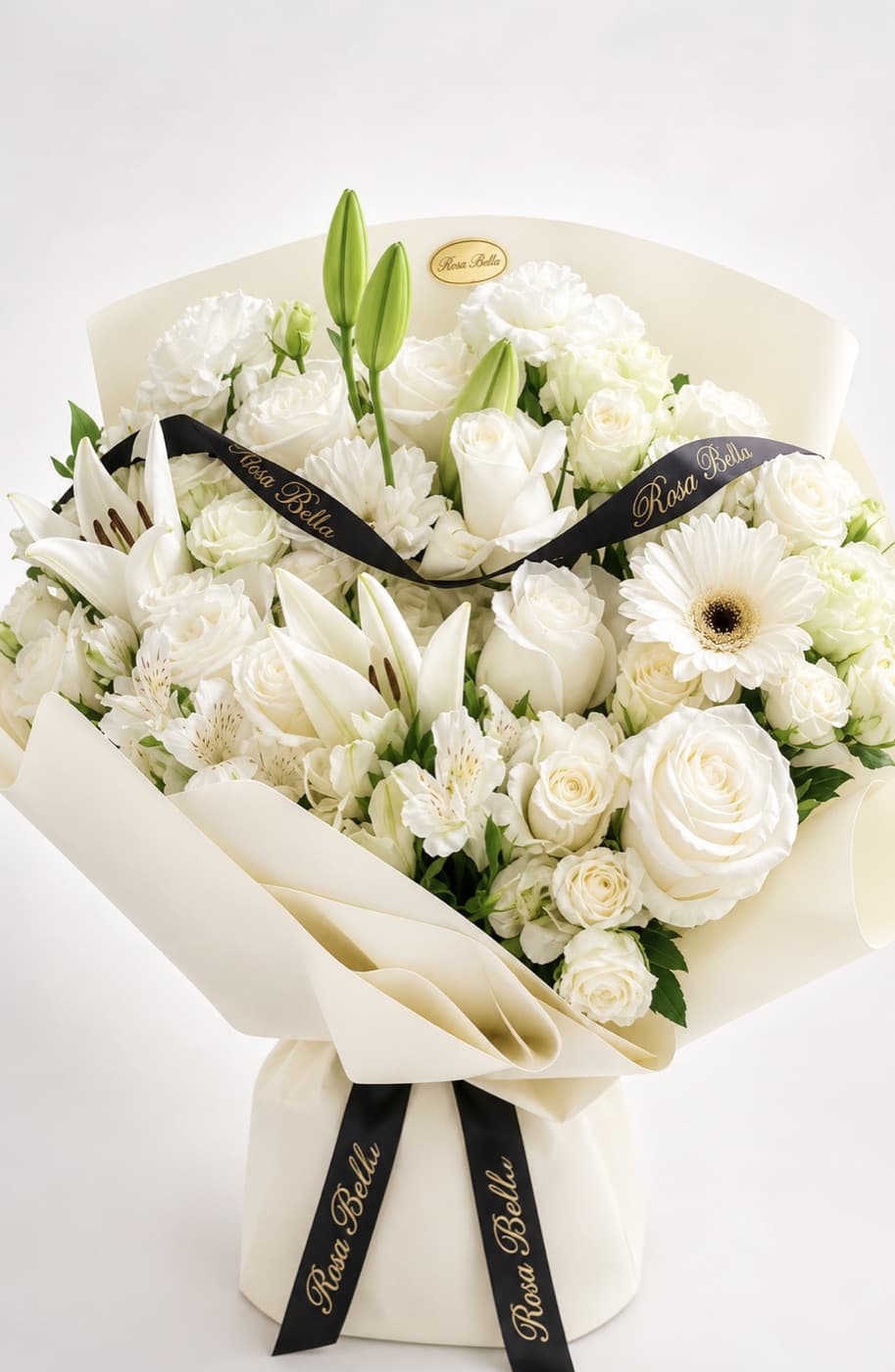 An all-white bouquet of lilies, roses and gerbera in cream paper with a black ribbon.
