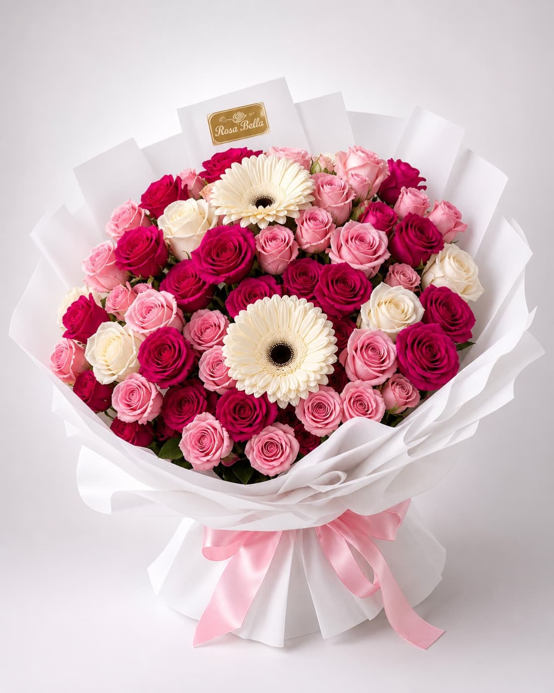 A bouquet of pink and magenta roses with two large white gerbera daisies, in white paper.