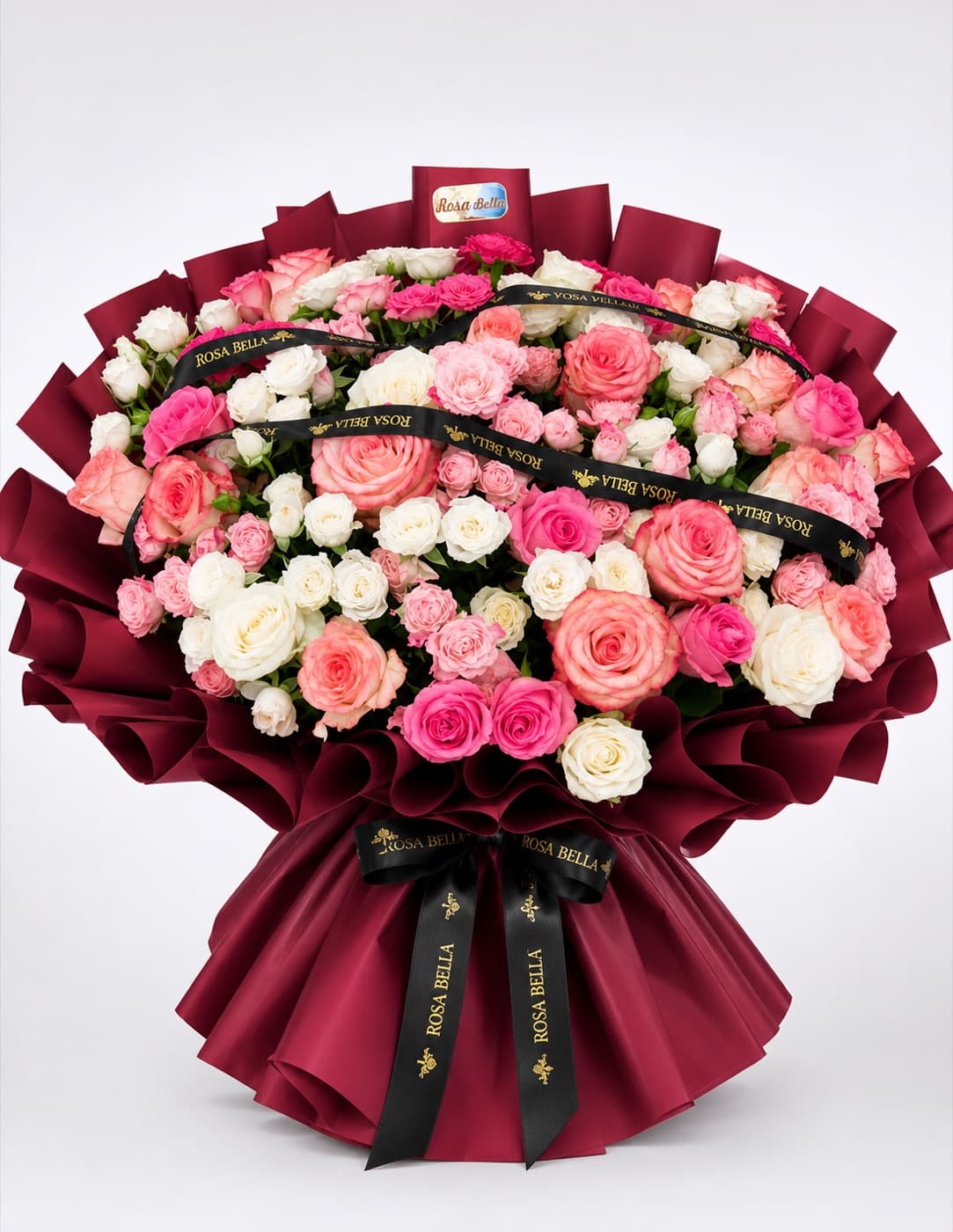 A very large bouquet of pink, peach and cream roses in deep burgundy wrapping.